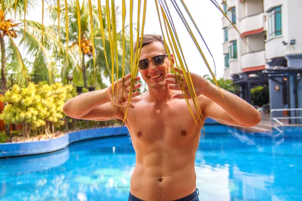 Yakışıklı Genç Adam Yüzme Havuzu kenarına eğilerek ve Tropikal İklim kamera gülümseyerek.