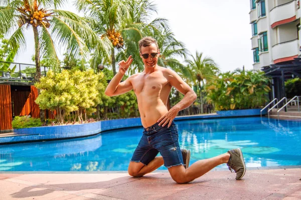 Yakışıklı Genç Adam Yüzme Havuzu kenarına eğilerek ve Tropikal İklim kamera gülümseyerek.