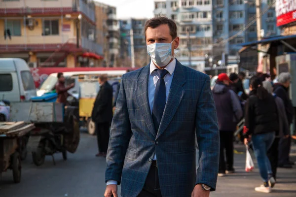 Caucasian business people working in Asia, in China. Business travel concept. Ecology in China, a young businessman in a mask on the street in Beijing.