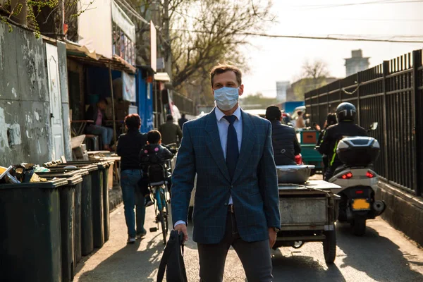 Caucasian business people working in Asia, in China. Business travel concept. Ecology in China, a young businessman in a mask on the street in Beijing.