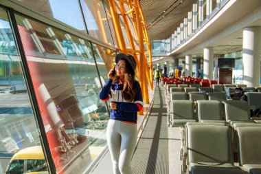 Asyalı kadın havaalanında cep telefonu kullanarak, pencereden dışarı bakıyor.