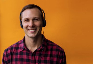 Genç mutlu yakışıklı adam kulaklık takıyor ve sarı arka planda müziğin tadını çıkarıyor..