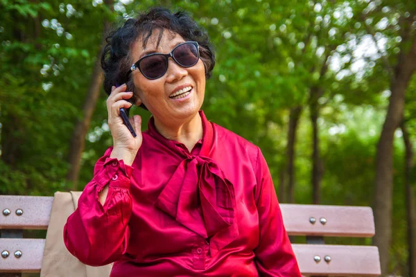Old asian woman using mobile phone and smilling in garden in the park. Happy Old asian businesswoman using smart phone and laptop in summer park.
