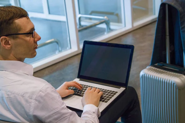 elinde dizüstü bilgisayar ve akıllı telefon ile havaalanı salonunda çalışan yakışıklı orta yaş adam. iş kavramı.