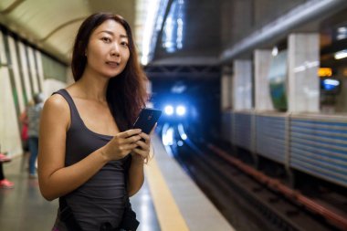 Genç güzel Asyalı kadın cep telefonuyla tren istasyonunda.