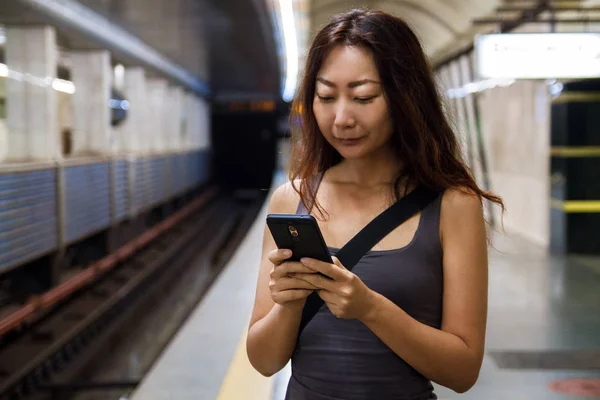 Young beautiful asian woman using mobile phone at train station.