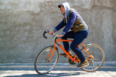 Kopya alanı ile sonbaharda şehirde gri bir duvarın önünde bisikletiyle duran gülümseyen bir genç adamın portresi.