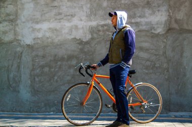 Kopya alanı ile sonbaharda şehirde gri bir duvarın önünde bisikletiyle duran gülümseyen bir genç adamın portresi.