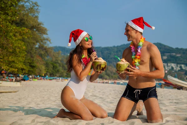 幸せなカップルは ココナッツとクリスマスの帽子で白い砂浜に座っています テキストのための場所と海の休暇の概念 — ストック写真