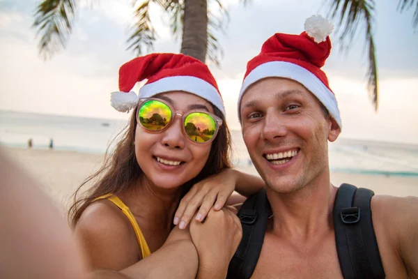 サンタクロースキャップの幸せなカップルは 海辺のビーチで自分撮りを取ります — ストック写真