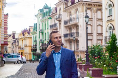 Kendinden emin genç işadamı şehirde cep telefonu kullanıyor. 