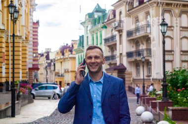 Şehirde telefon kullanarak gülümseyen yakışıklı işadamı.