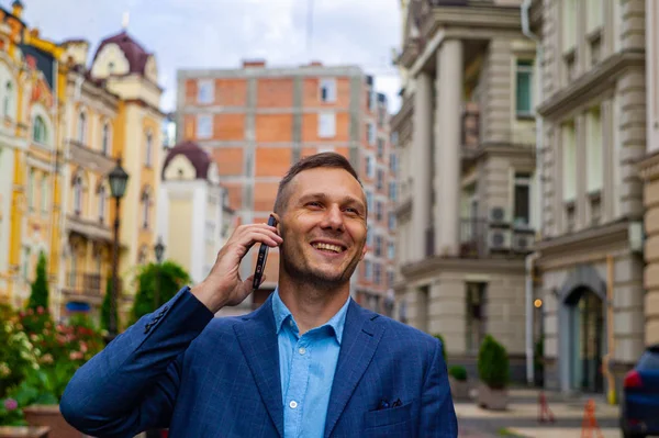 Smiling handsome businessman using phone in city.