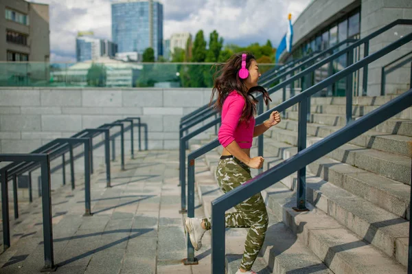 腰起描绘快乐的年轻亚洲妇女训练 她正在听耳机的音乐 看着智能手机 运动员站在户外微笑 — 图库照片