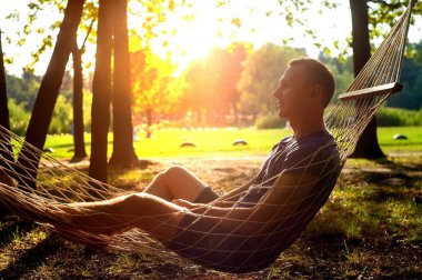 Altın sonbahar gününde hamakta oturan adam.
