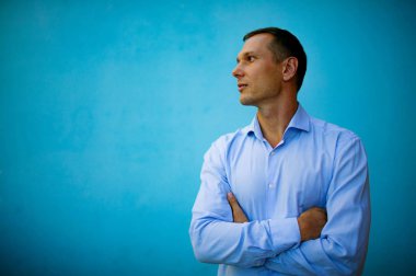 Mavi bir arka plan önünde duran kendine güvenen yakışıklı genç adam. 