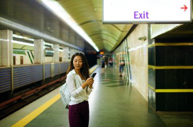 Cep telefonunu metro platformda kullanan güzel kadın. Ulaşım kavramı.