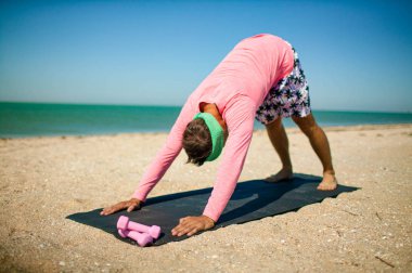 Genç sportif adam plajda çekirdek kasları eğitim. Komik erkek atlet Deniz yakınlarındaki paspas üzerinde çalışıyor.