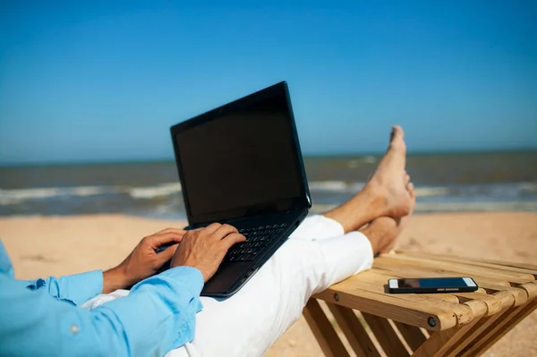 gün batımında sahilde şezlongda yatan dizüstü bilgisayar üzerinde çalışan adam