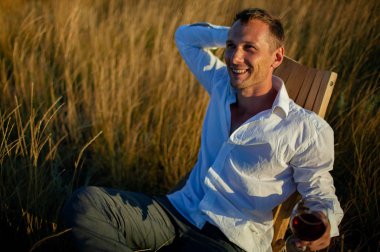 Yakışıklı olgun adam gün batımında açık kırmızı şarap cam tatma.