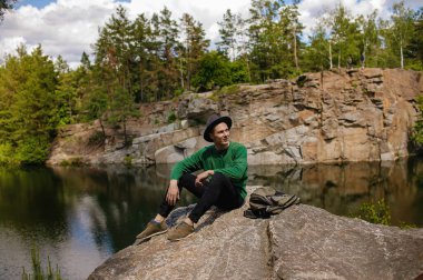 Sonbaharda bir gölün manzarasına hayran olan, kayadaki şapkalı yakışıklı bir adam..