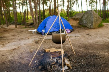 Yiyecek, sonbahar ormanında kamp ateşinde konteynırda pişiriliyor.