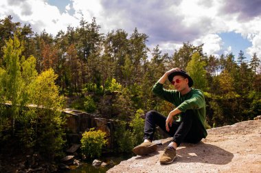 Sonbaharda bir gölün manzarasına hayran olan, kayadaki şapkalı yakışıklı bir adam..