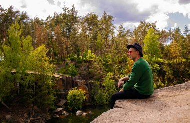 Sonbaharda bir gölün manzarasına hayran olan, kayadaki şapkalı yakışıklı bir adam..
