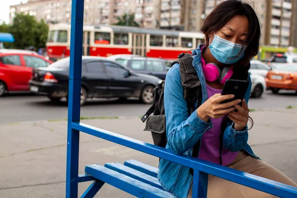 Chinese Woman Waiting For Bus At Bus Stop In City Street And Wearing Face Mask
