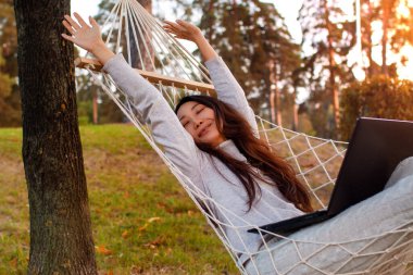 Genç Asyalı Kadın Sonbahar Parkı 'nda Hamakta Dizüstü Bilgisayar Kullanıyor.
