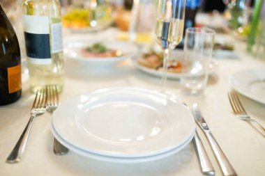 Beyaz masa ayarları. Zarif boş tabak, çatal bıçak, peçete ve cam..