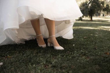 Gelinin bacakları çimlerin üzerinde yüksek topuklu ayakkabılarla