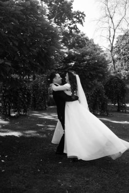 Gelin ve damat parkta kucaklaşıyor, siyah ve beyaz fotoğraf. 