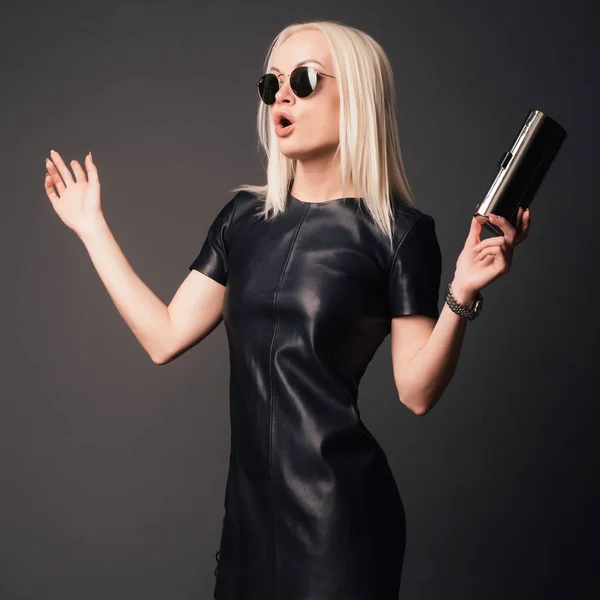 surprised stylish woman in black leather dress with small silver bag and watch. fashion concept.