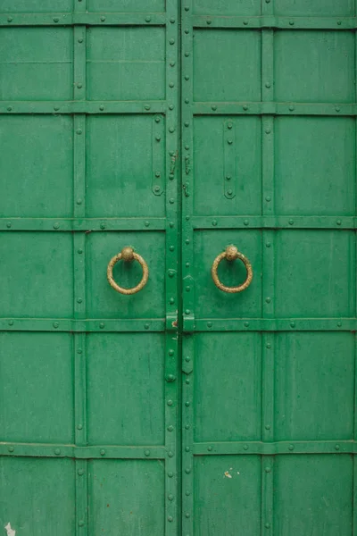 large antique wooden green doors with ring-shaped handles.