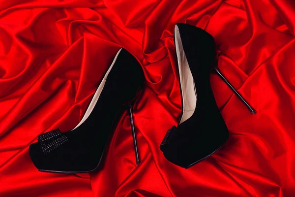 High-heeled shoes lying on red satin, can use as background