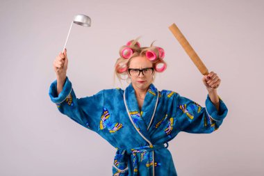 onun elinde bir kepçe ile bir sabahlık ve curlers sert ev kadını.