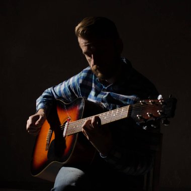 ekose gömlekli bir adam portresi bir füzyon elektro-akustik gitar çalar. Düşük anahtar portre.