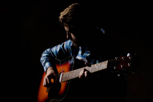 High contrast portrait of bearded man in plaid shirt playing acoustic guitar.