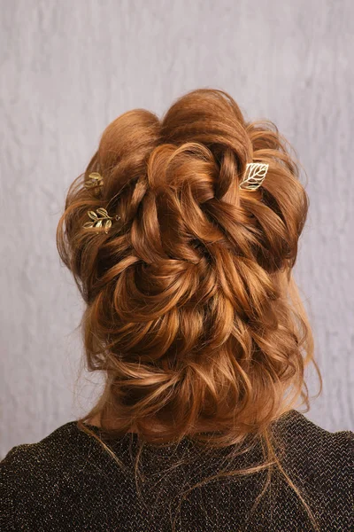 Hairstyle Greek braid on the head of a red hair woman back view close-up on a gray background.Fashionable professional women's hairdo.