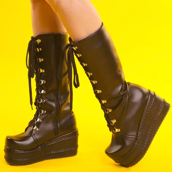 Female legs in black army boots isolated on yellow background