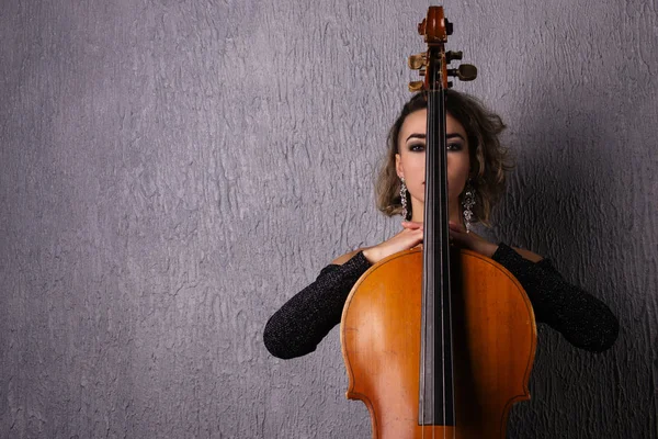 Portrait of a young sad woman. Part of the face is covered by the neck of the cello.