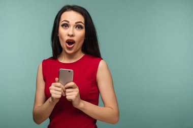 Heyecanlı gülen kadın ayakta ve cep telefonuyla mavi arka plan üzerinde - görüntü kırmızı elbiseli