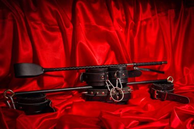 BDSM kıyafet kadar kapatın. Esaret, garip yetişkin seksi oyunlar, ilginçlik ve Bdsm yaşam tarzı konsepti ile bir çift deri kelepçe, flogger, kamçı kopya alanı ile kırmızı ipek.