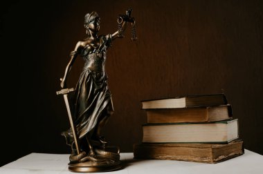 Beyaz ahşap bir masa yanında bir yığın üzerinde Themis heykelcik duruyor eski kitaplar.