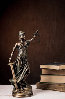 Beyaz ahşap bir masa yanında bir yığın üzerinde Themis heykelcik duruyor eski kitaplar.
