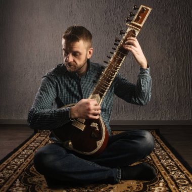 Portrait of a European man playing the sitar sitting on the carpet clipart