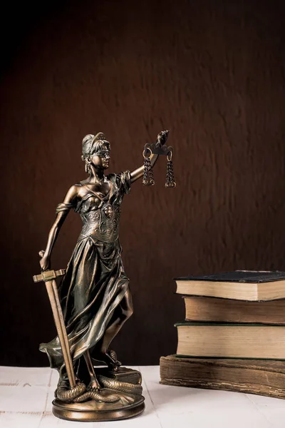 Estatuilla de Themis está parada en una tabla blanca de madera al lado de una pila de libros viejos . —  Fotos de Stock