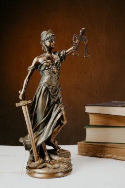 Beyaz ahşap bir masa yanında bir yığın üzerinde Themis heykelcik duruyor eski kitaplar.