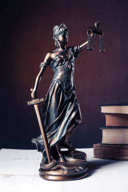 Beyaz ahşap bir masa yanında bir yığın üzerinde Themis heykelcik duruyor eski kitaplar.